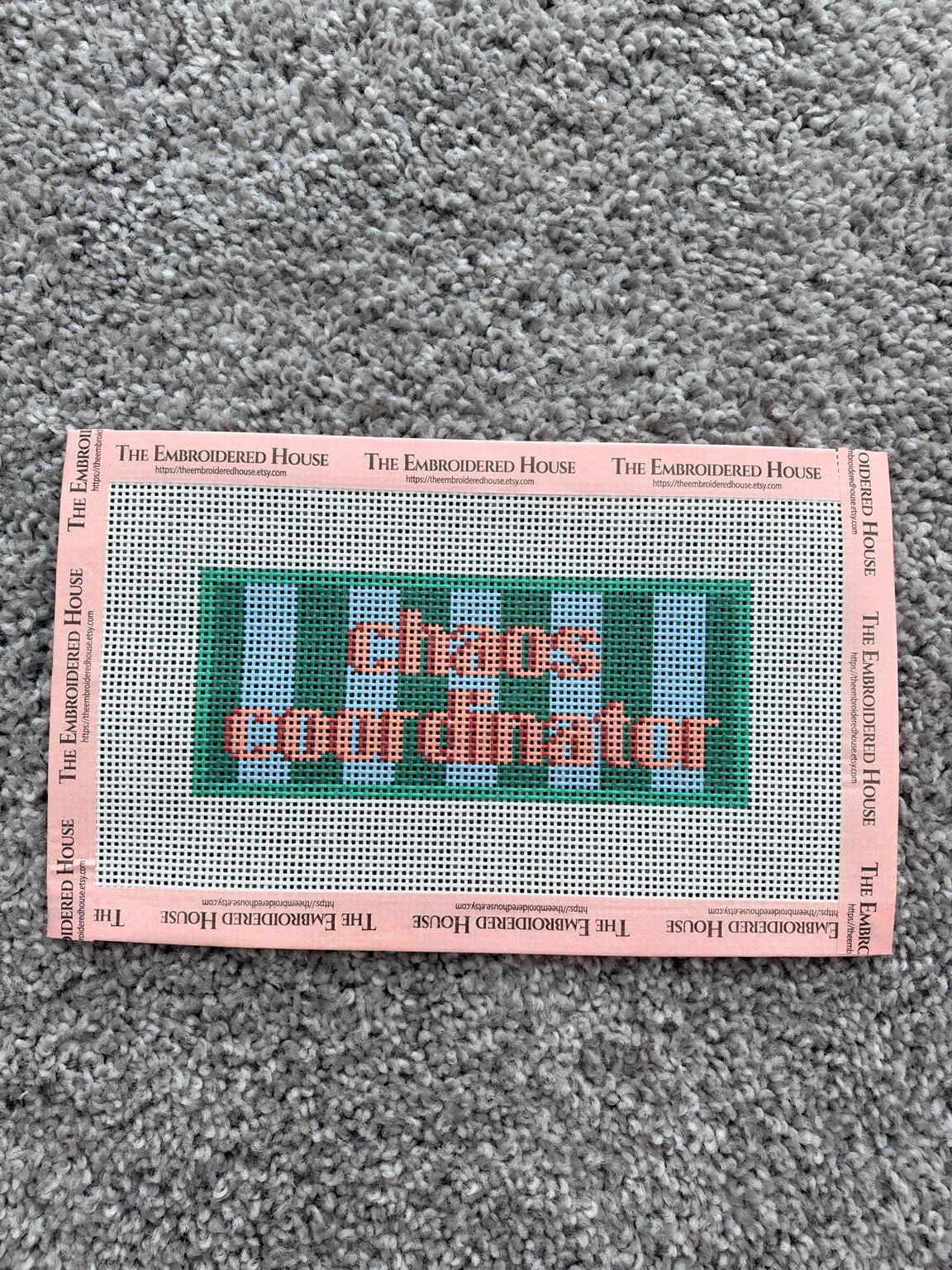 Chaos Coordinator printed needlepoint canvas with coral lettering, green and light blue stripes, and pink branded tape
